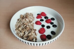 Yogurt, blueberries, raspberries and granola in a white bowl on a wooden background.