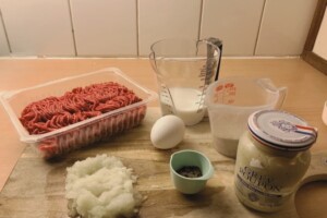 Ingredients to make Swedish meatballs are presented on wooden table.