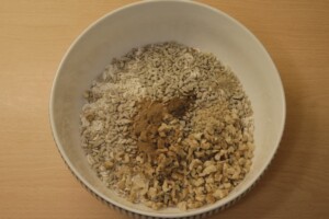 In a large mixing bowl there are oats, walnuts, sunflower seeds, and spices.