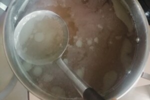 A fine mesh skimming tool is used to remove impurities from the chicken stock.