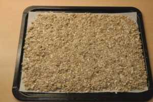 Granola mixture is evenly spread onto the prepared baking sheet.