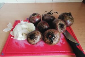 Beets washed under cold water and are now on a red cutting board along with garlic.