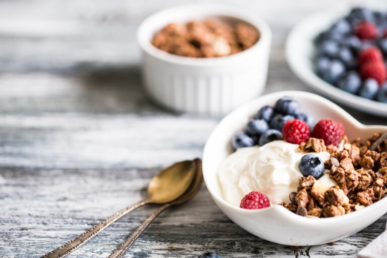 Greek yogurt, blueberries, raspberries and granola in a white bowl on a wooden background.