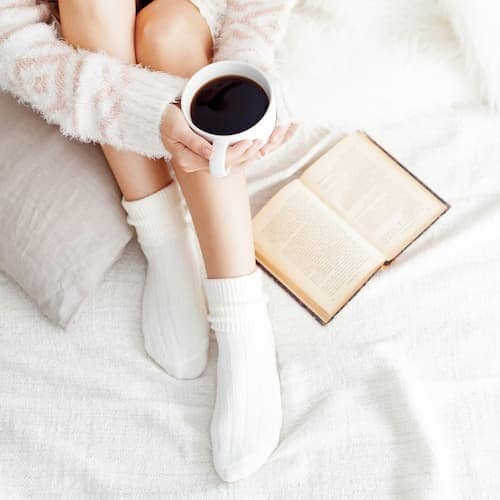 Soft photo of woman on the bed with an old book and a cup of coffee. Picture for About Us.