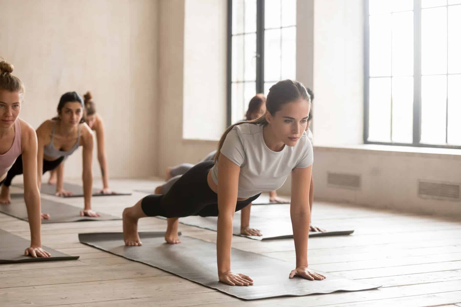 A group of people in a studio perform plank poses on yoga mats, highlighting core strength and the benefits of yoga.