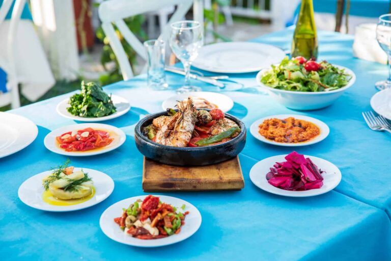 A table set by the sea displays an array of nutritious foods, exemplifying the Blue Zone Diet's avoidance of ultra-processed foods.