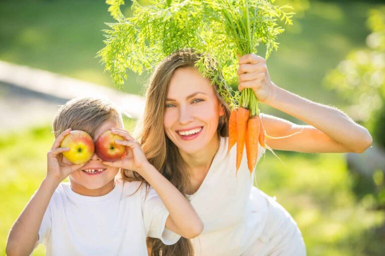 Family clean eating for beginners concept. Mother and son having fun outdoors with carrots and apples.