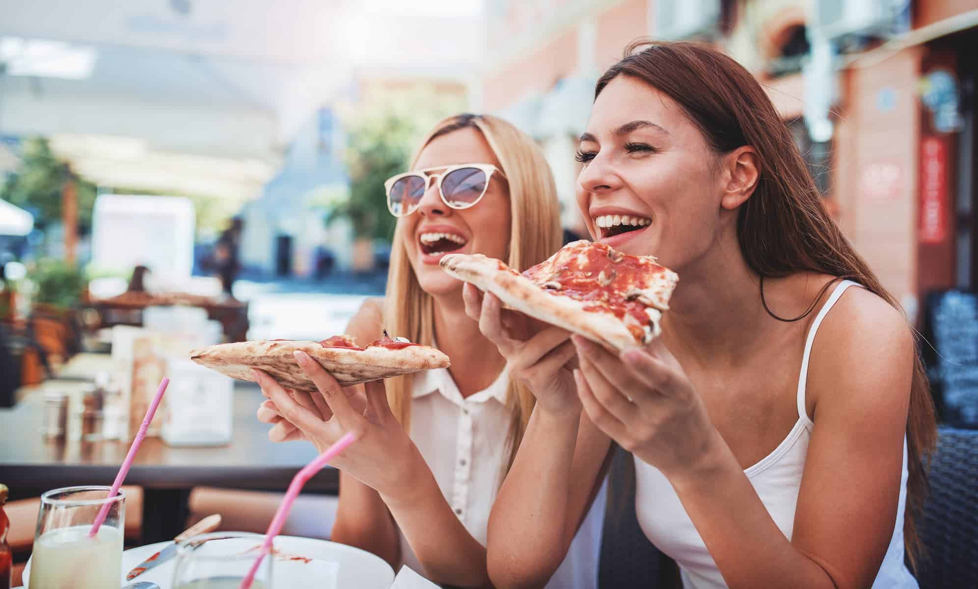 Two happy women eating modern food at the mall that is unhealthy.