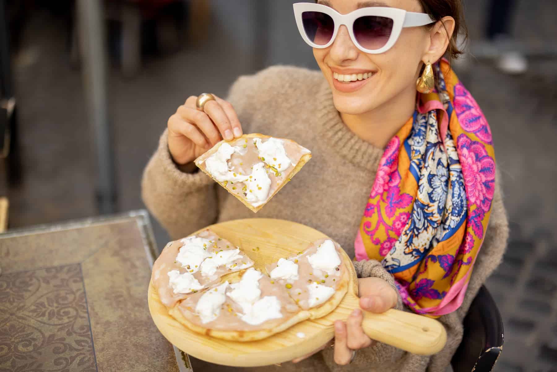 Happy young woman having pizza without feeling fear of eating carbs.