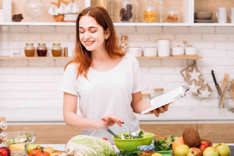 Young female in the kitchen with a book in her hand, preparing nutritious lunch because she has healthy relationship with food.