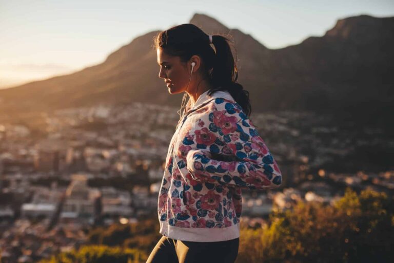 Ponytailed woman enjoys mountain scenery with earbuds, reflecting active engagement in a healthy lifestyle for mental wellness.