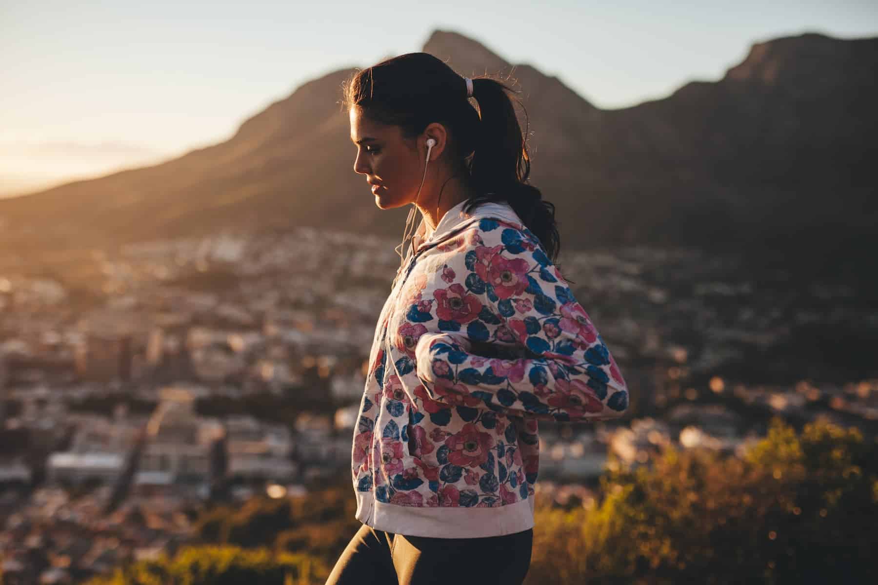 Ponytailed woman enjoys mountain scenery with earbuds, reflecting active engagement in a healthy lifestyle for mental wellness.