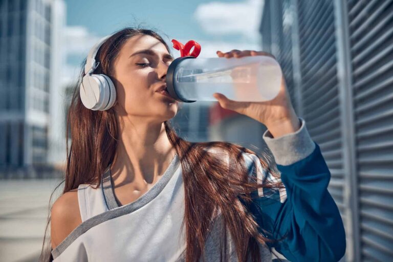 A woman wearing headphones drinks from a water bottle, demonstrating hydration as part of habits of a healthy lifestyle.