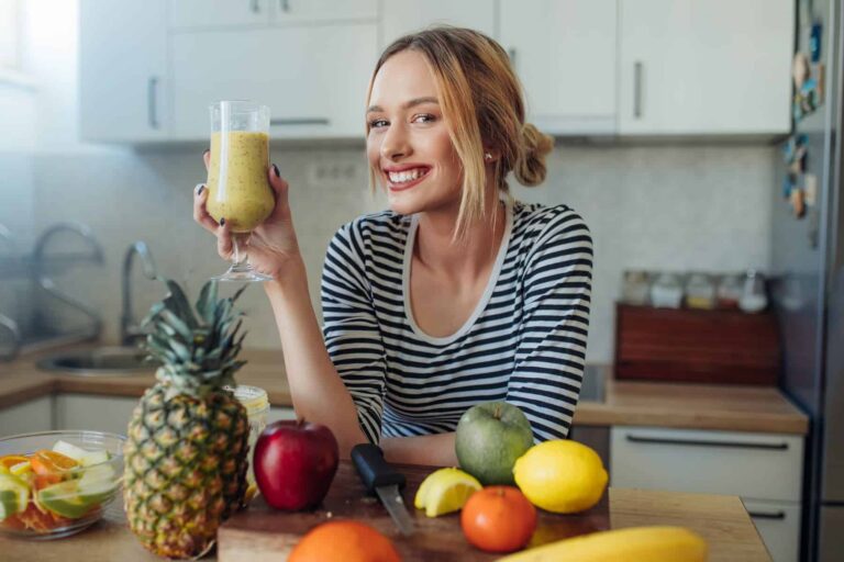 A happy, healthy woman enjoys a smoothie in her kitchen, embracing simple daily habits as she learns how to lose weight sustainably.