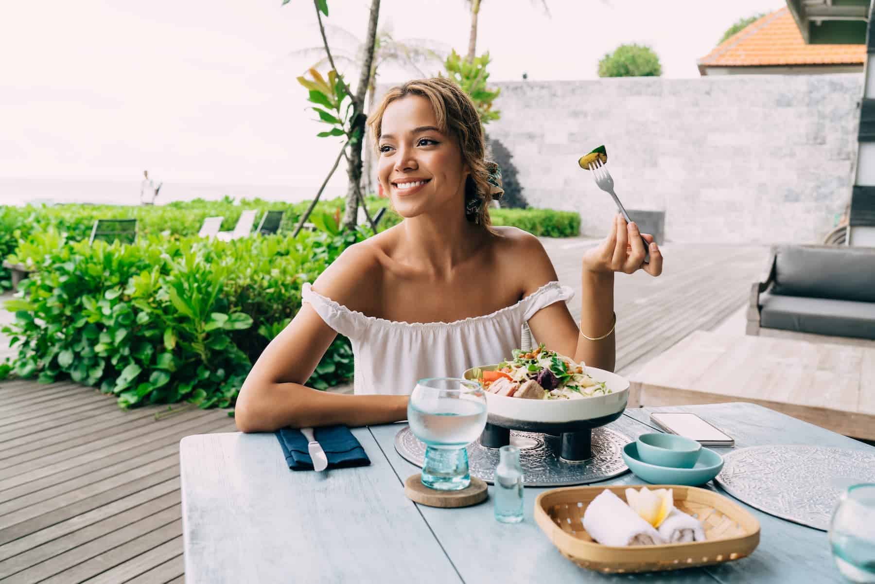 Young woman seated outside enjoying a nutritious salad. She knows how to make intuitive eating work for her weight loss goals.
