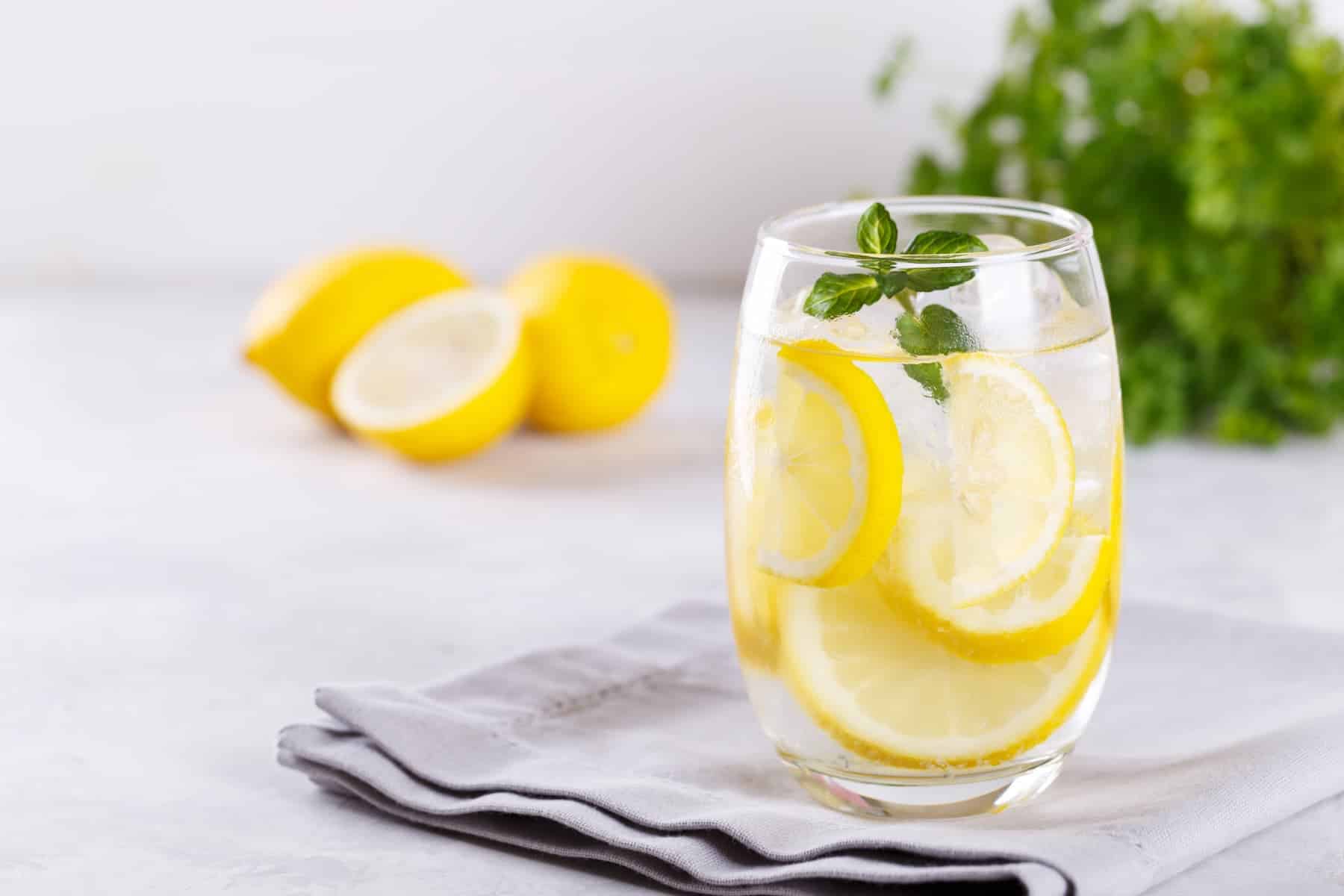 A glass of lemon water with mint on a gray napkin, highlighting lemon water risks such as enamel erosion when consumed too often.
