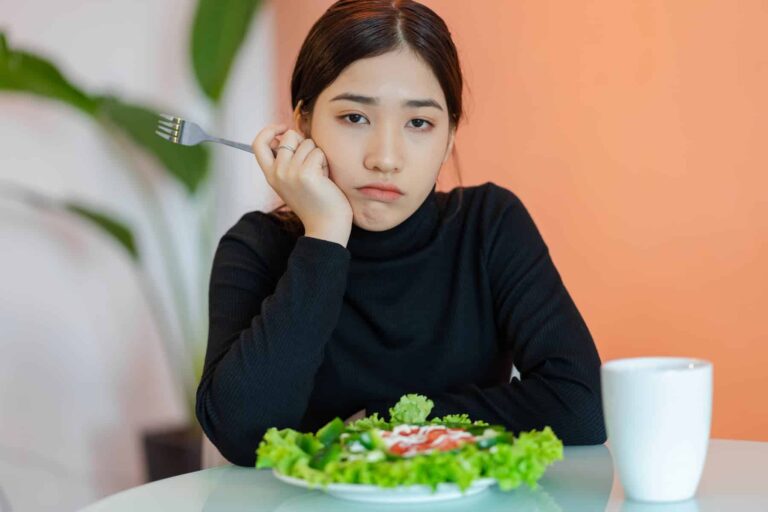 Sad young woman in front of a green salad plate thinking about how maintaining weight loss is so difficult.