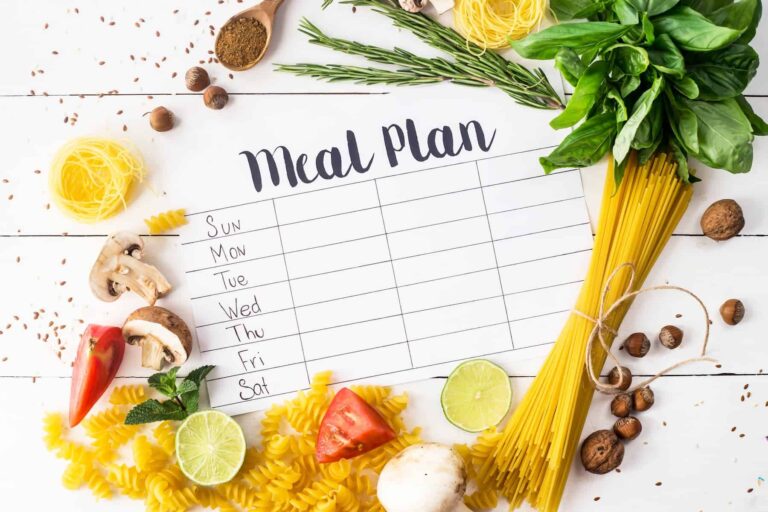 Spaghetti, nuts, mushrooms, greens, and a meal plan on a white background, showcasing how to start meal planning for beginners.