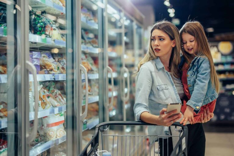 Woman carrying her daughter in grocery store is pondering about the difference between processed food vs ultra-processed foods.