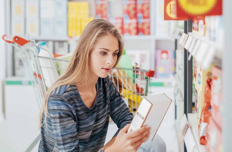 At the grocery store, a woman reads food labels attentively, demonstrating her understanding of the link between hidden sugar and obesity.