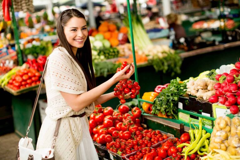 A young woman explores the market amidst fresh vegetables, feeling excited as she rediscovers real food in a world dominated by ultra-processed convenience.