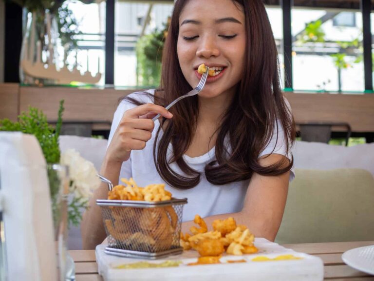 Happy woman indulging in salty fried food at a restaurant, wondering why she has constant salt cravings.