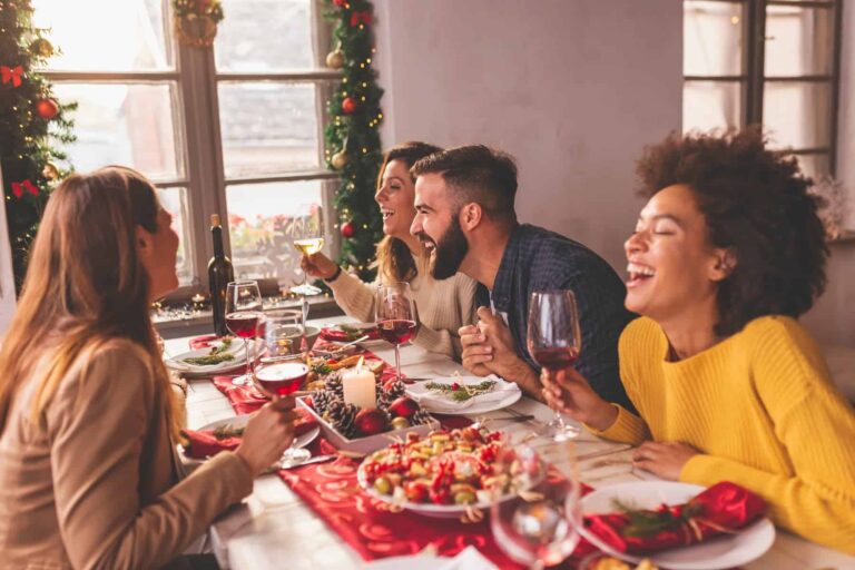 Friends celebrating Christmas around a table with food, red wine, and healthy homemade snacks, showcasing tips for a healthier holiday eating.