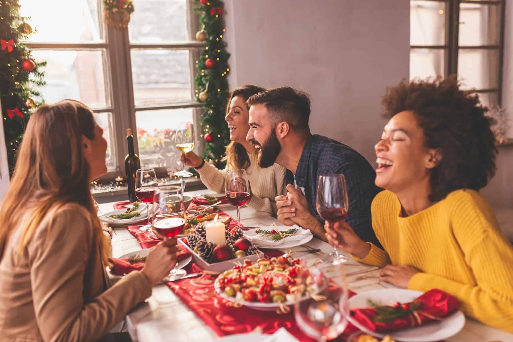 Friends celebrating Christmas around a table with food, red wine, and healthy homemade snacks, showcasing tips for a healthier holiday eating.