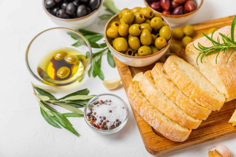 Assorted olives and olive oils in bowls with ciabatta bread on a cutting board, perfect for showcasing types of olive oil.