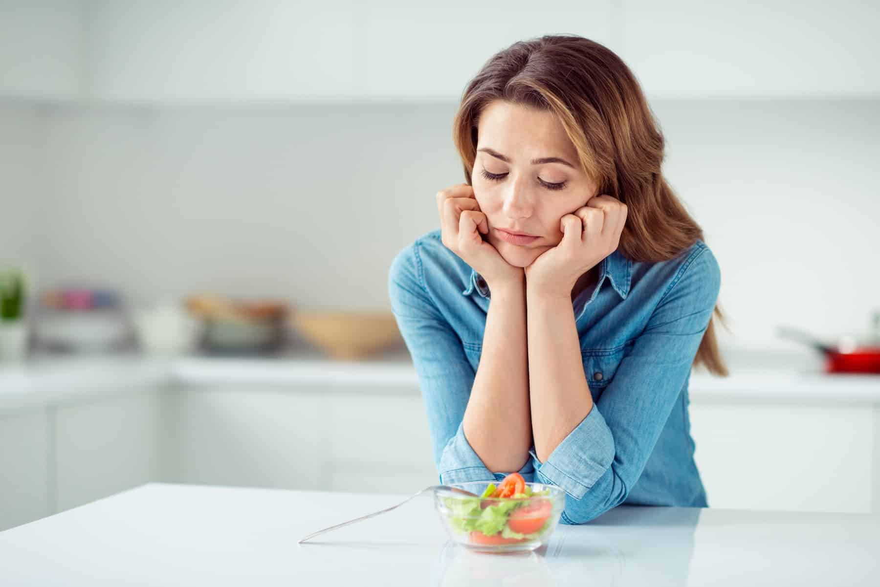 A woman feeling frustrated in her kitchen, unaware that undereating is slowing her metabolism and that the 'calories in, calories out' concept isn't the full solution.