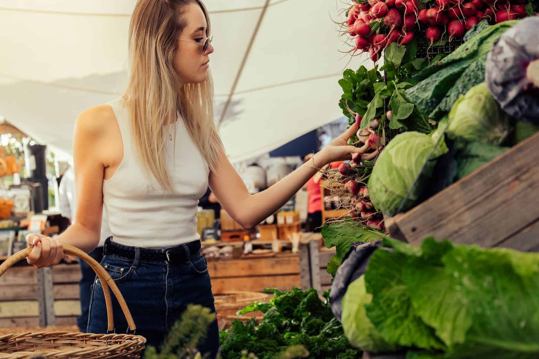 Young blonde woman with a basket shopping for healthy food to target lower belly pooch at a market.