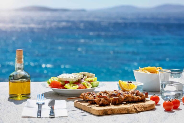 A Greek food scene featuring a fresh salad and a bottle of olive oil, set against the stunning Aegean Sea—highlighting the health benefits of olive oil.