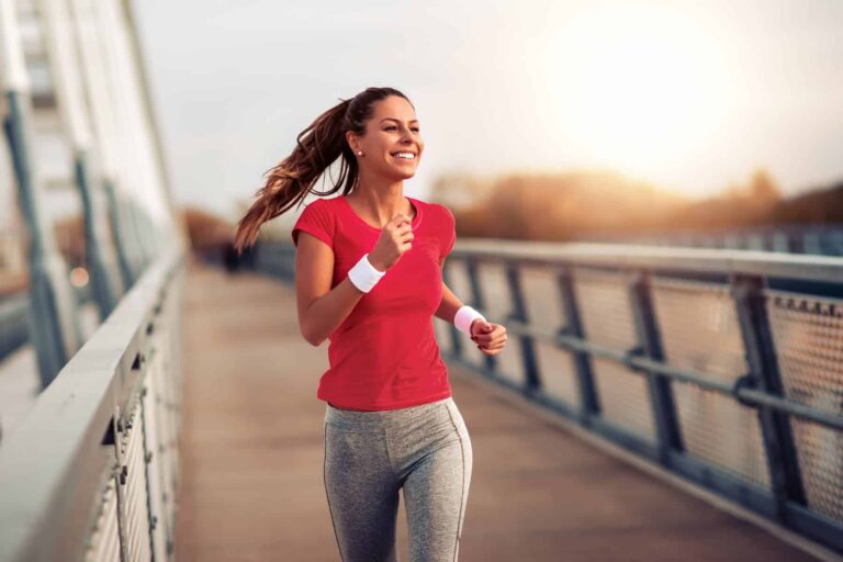 A fitness woman in a red t-shirt jogs outdoors during sunset, practicing healthy habits to start the new year.