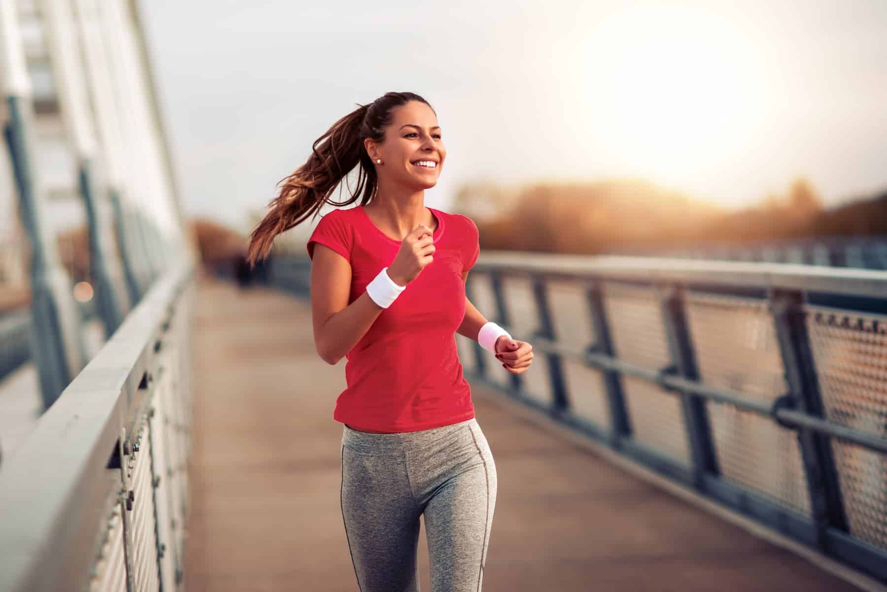 A fitness woman in a red t-shirt jogs outdoors during sunset, practicing healthy habits to start the new year.
