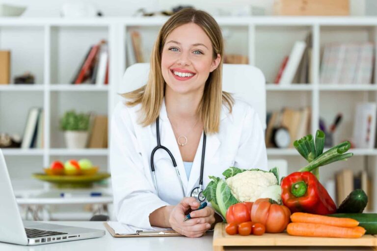 A nutritionist smiles in her office with healthy prebiotic foods, like fresh vegetables, next to her.