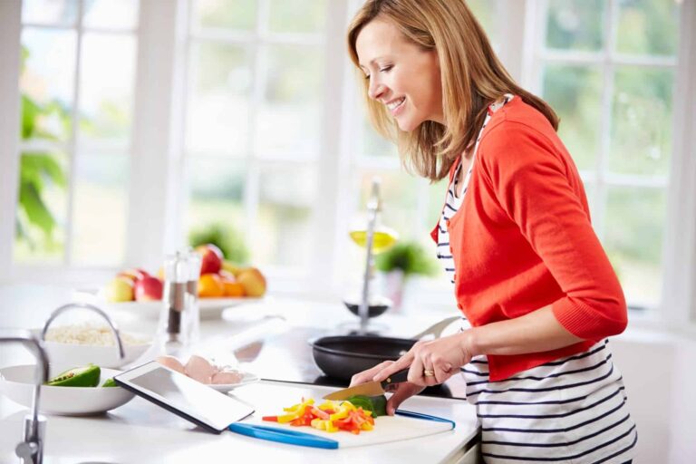 A woman follows a Mediterranean diet guide for beginners on her iPad while chopping peppers in her kitchen.