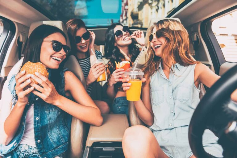 Friends enjoy their lunch in the car, which consists of sugary drinks, hamburgers, and fries instead of real food.