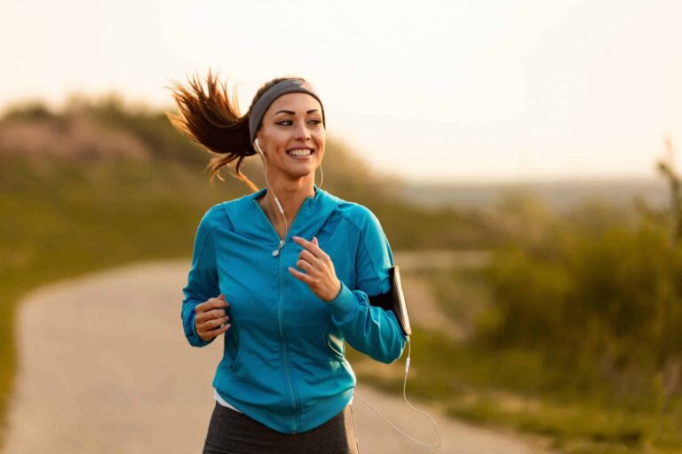 A woman in athletic wear runs outside with headphones and an armband, embracing fitness as part of a healthy lifestyle.