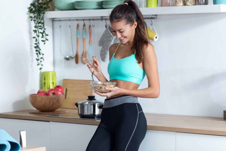 A sporty young woman eating a bowl of muesli in her kitchen, understanding the importance of healthy eating for weight loss.