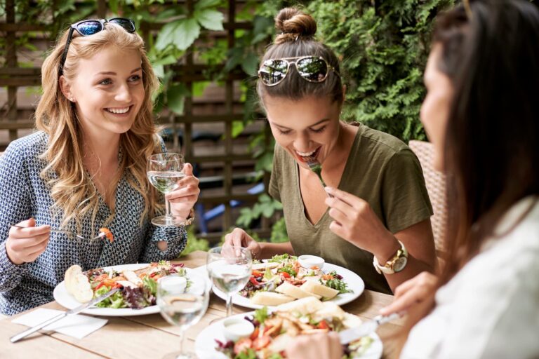 Woman enjoying a healthy chicken salad and drinking water while eating outdoors with friends, showing how to lose weight without dieting.