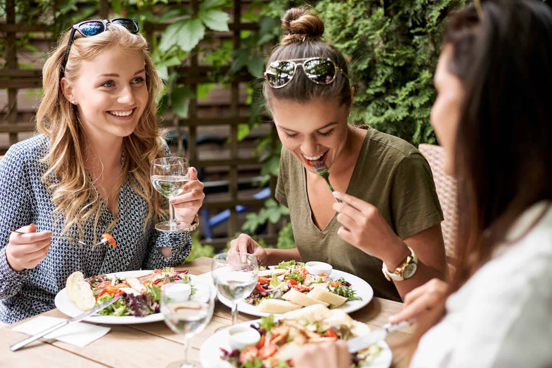 Woman enjoying a healthy chicken salad and drinking water while eating outdoors with friends, showing how to lose weight without dieting.