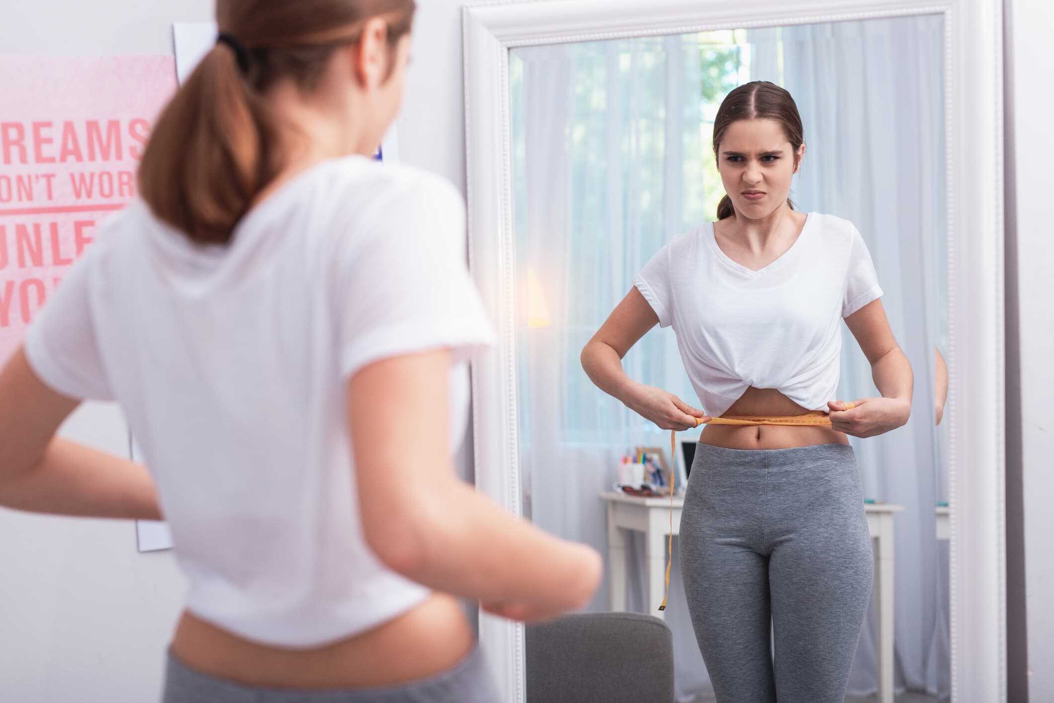 Teen girl measuring her lower belly with a tape measure, unsure of the cause of her belly pooch.