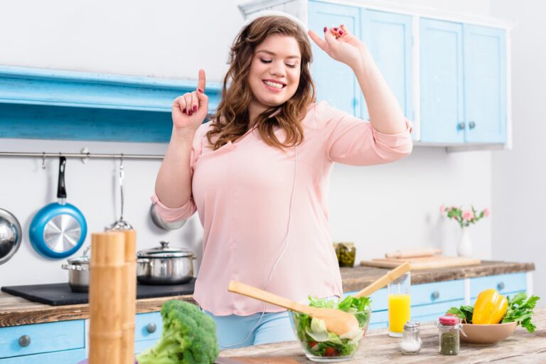 Happy woman preparing a fresh salad in her kitchen while listening to music, enjoying healthy food choices as part of her weight loss journey.