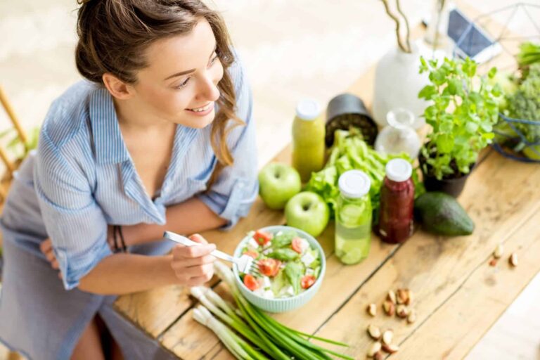 A woman eating a colorful salad with fresh ingredients and smoothies, illustrating balanced meals from an anti inflammation diet.