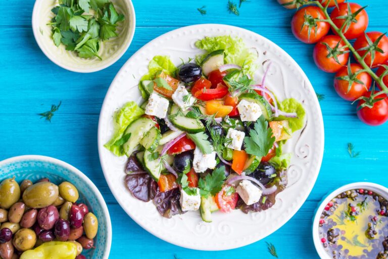 Salad with olive oil, olives, tomatoes, and feta cheese on a blue wooden table, representing a Blue Zones-style diet.