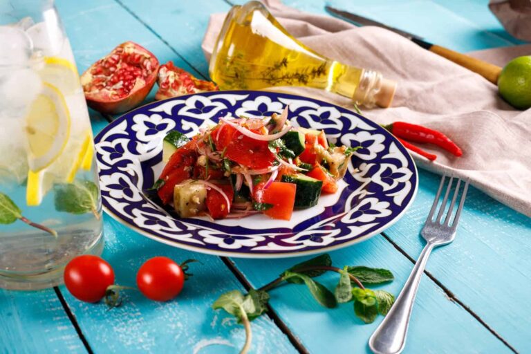 Healthy salad with olive oil, tomatoes, and fruit on a blue wooden table.