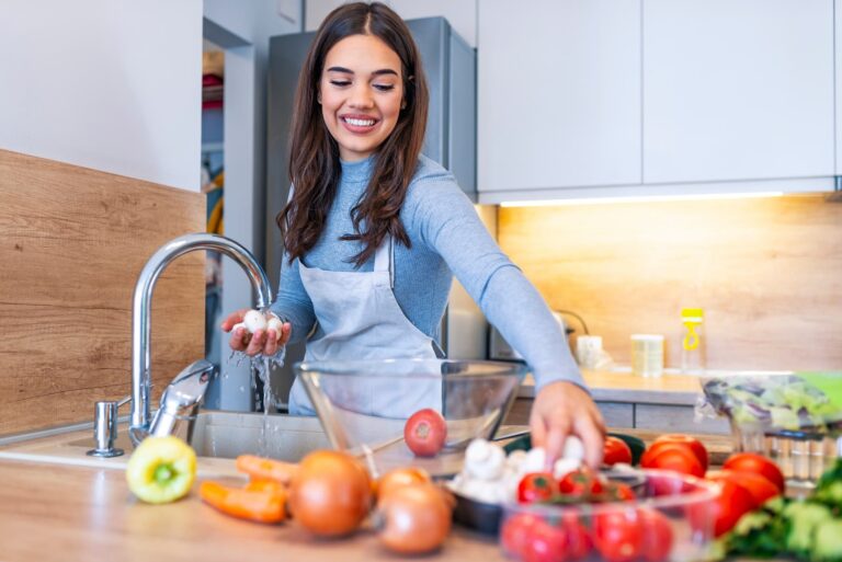 A woman wearing an apron washes fresh mushrooms in the kitchen, illustrating a step in preparing meals from an anti-inflammation diet food list.
