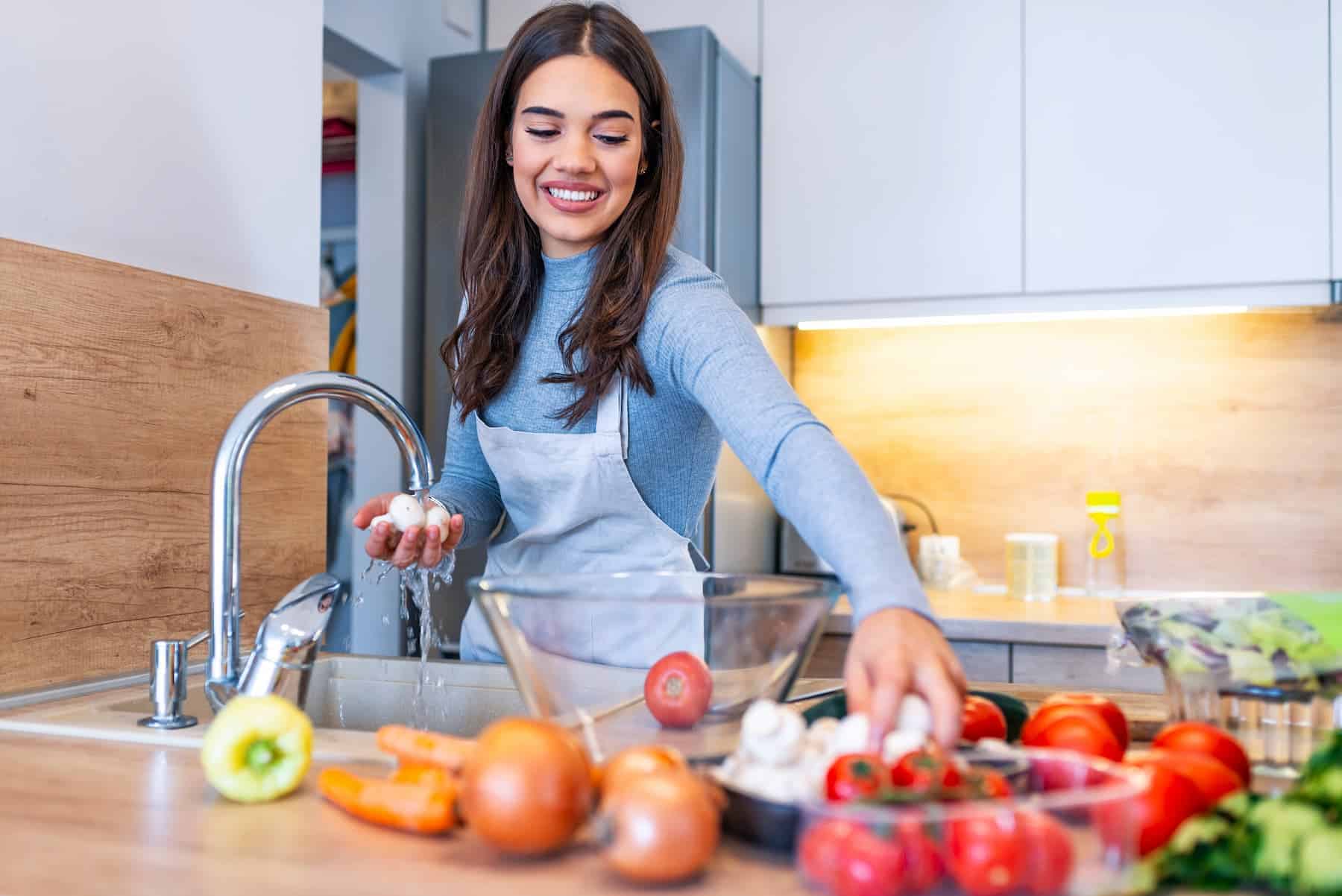 A woman wearing an apron washes fresh mushrooms in the kitchen, illustrating a step in preparing meals from an anti-inflammation diet food list.