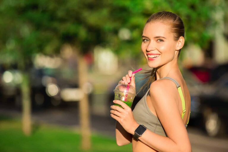 After completing a run, a woman in workout clothes enjoys an anti-inflammation smoothie outdoors on a sunny day.