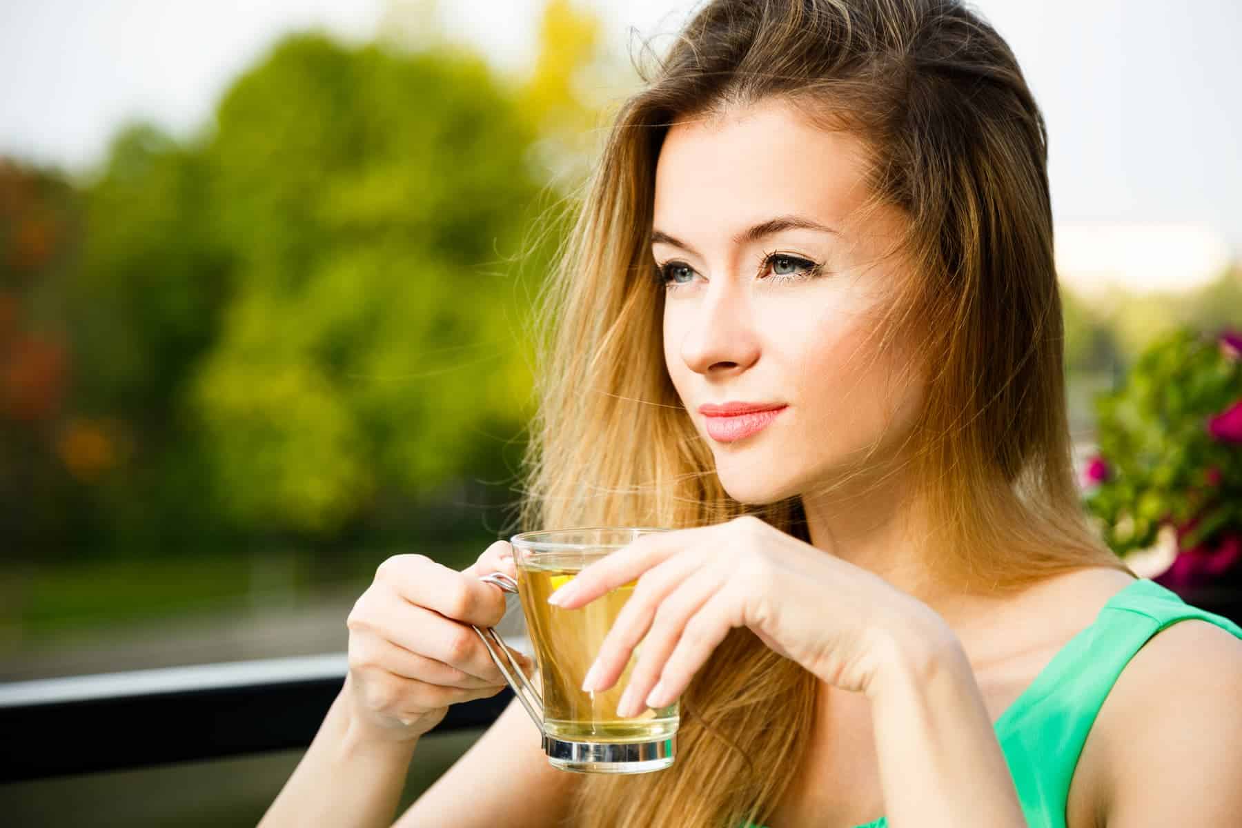 A woman sits on her balcony sipping anti-inflammation tea, appreciating the scenery and maintaining her healthy lifestyle.